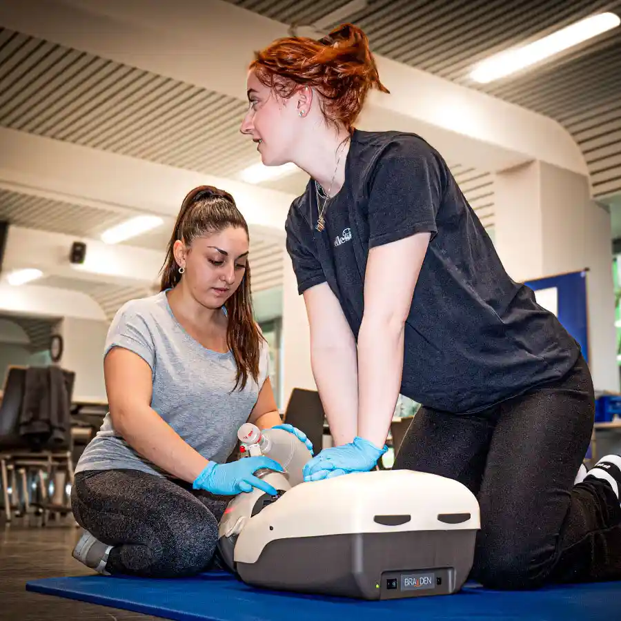 Zwei Studentinnen der HFGS sitzen vor einer Puppe und üben Herzmassage und Beatmen